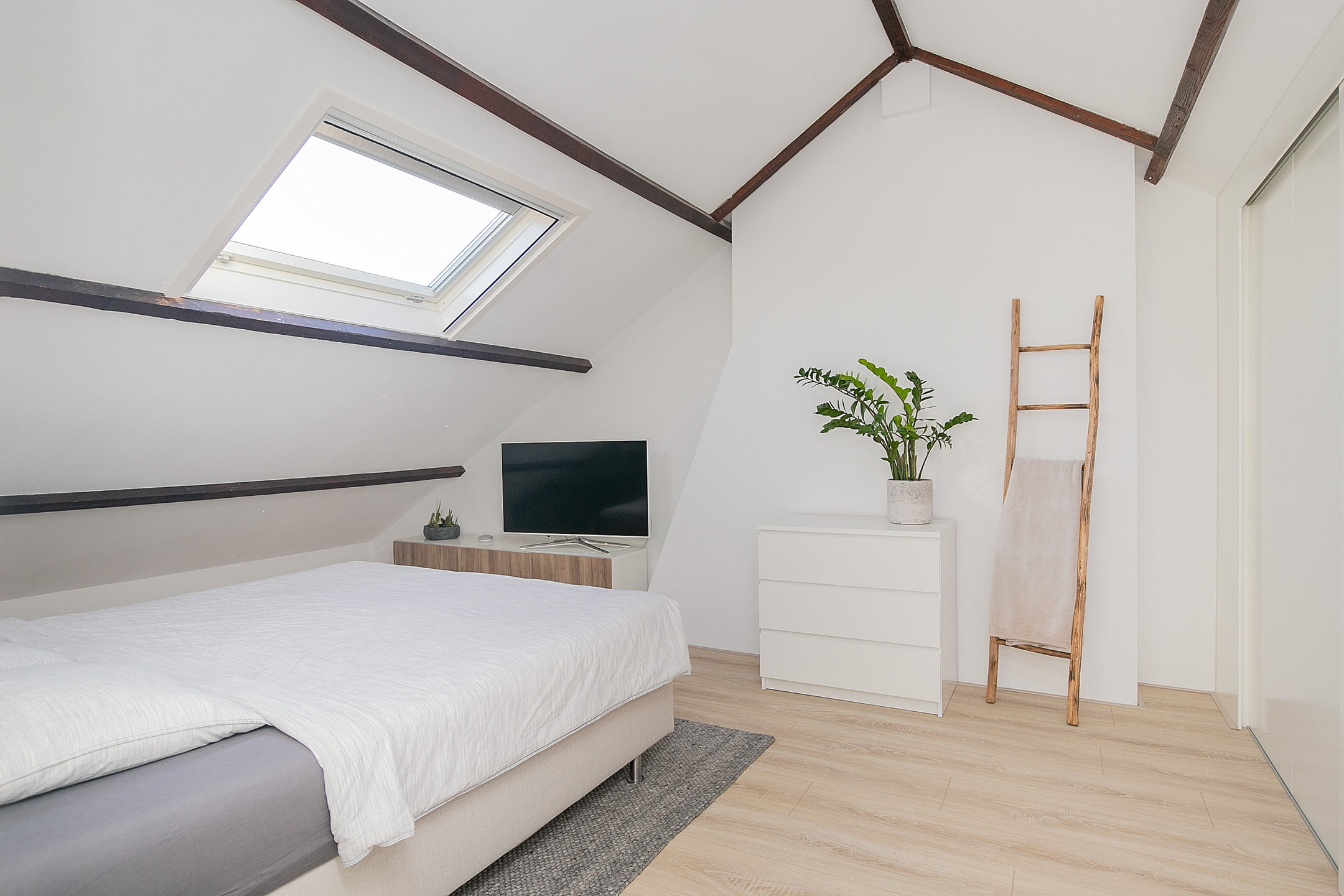 Lichte slaapkamer met houten balken, boxspring bed en ingebouwde kledingkast met schuifdeuren